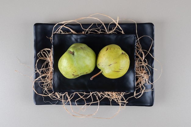 Free photo a stack of pears, black platters and straw on marble