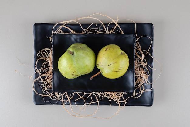 A stack of pears, black platters and straw on marble 