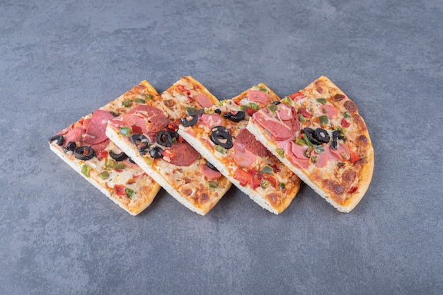 Stack of pepperoni pizza slices on grey background.