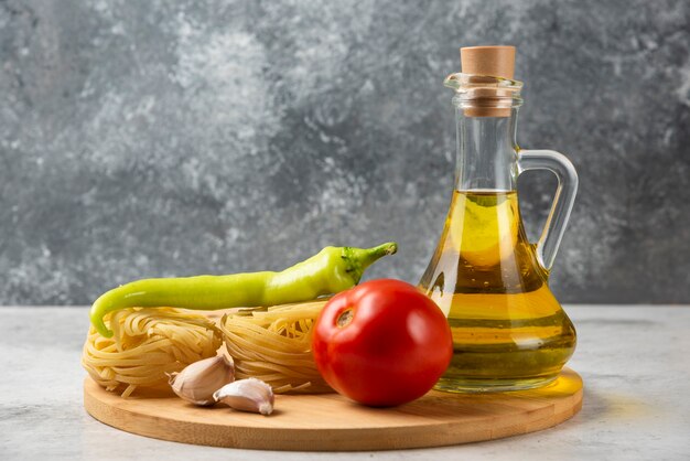Стек сырых гнезд макаронных изделий, бутылка оливкового масла и овощей на белом столе.