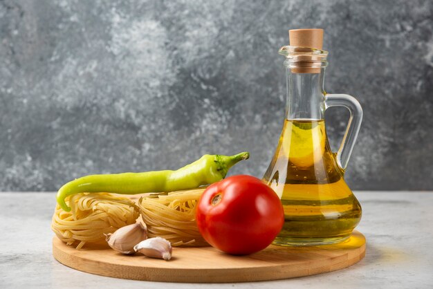 Stack of raw pasta nests, bottle of olive oil and vegetables on white table. 