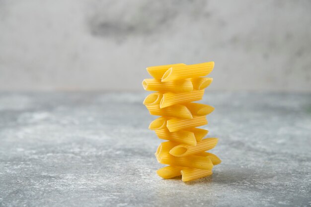 Stack of raw penne pasta isolated on marble background. 