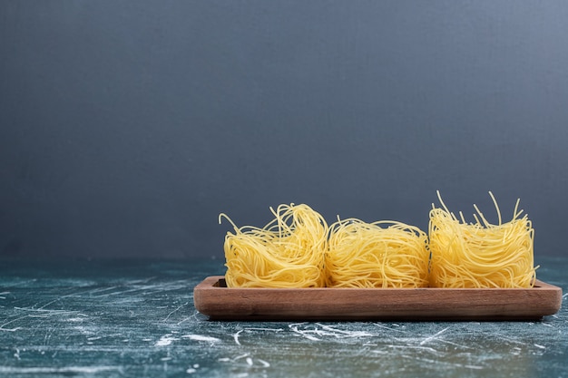 Pila di nidi di spaghetti crudi su tavola di legno. foto di alta qualità