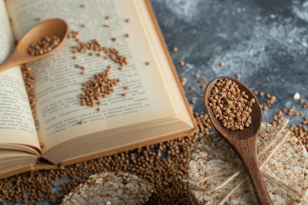 Stack of rice cakes , book and uncooked buckwheat on marble surface