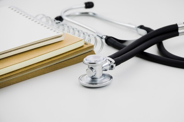 Stack of spiral notepad and stethoscope on white backdrop