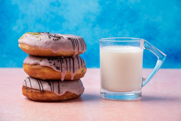 Free photo stack of strawberry donuts and a glass of milk on pink table.