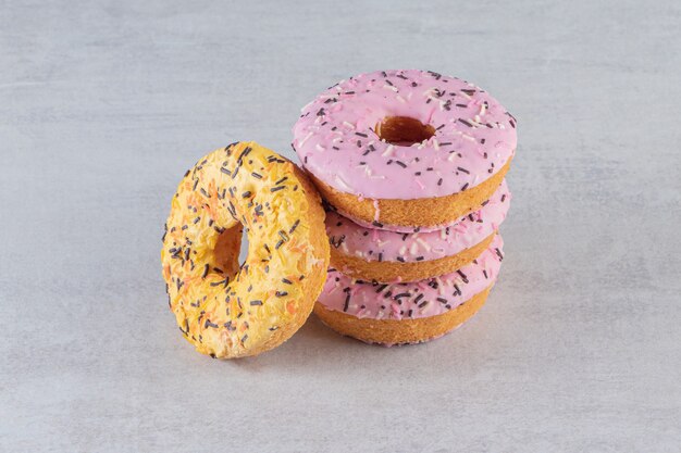 Stack of sweet donuts decorated with sprinkles on stone table. 