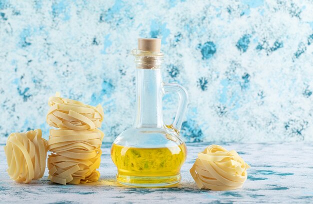 Stack of tagliatelle nests and glass of olive oil on blue.