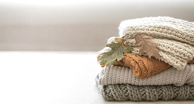 Stack of warm knitted items from autumn wardrobe close up on blurred white space copy space.