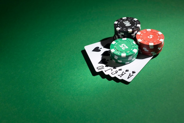 Stacked casino tokens and royal flush on green background