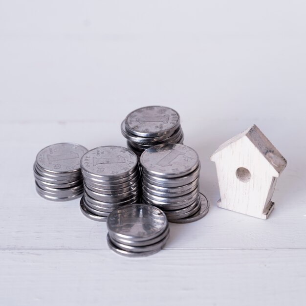 Stacked of chinese coin one yuan with miniature wooden birdhouse on wooden backdrop