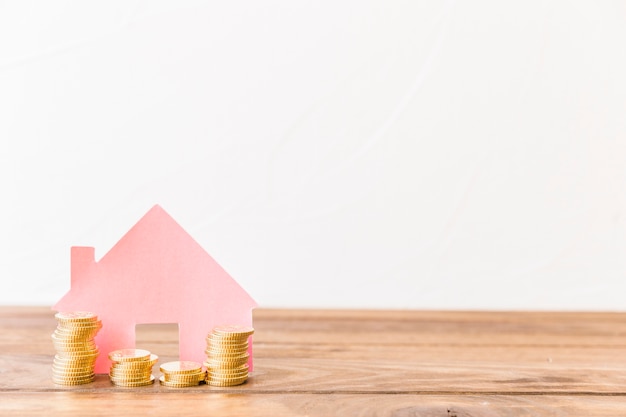 Stacked coins in front of house on wooden desk