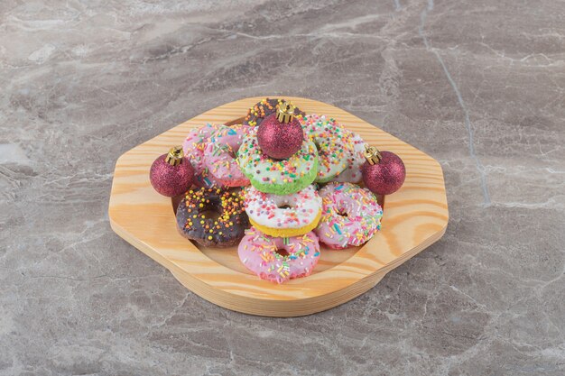 Stacked donuts and christmas baubles on a wooden platter on marble surface