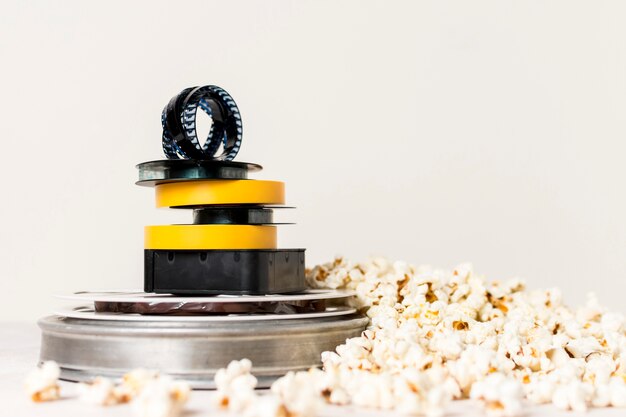 Stacked of film reels with film strip on top near the popcorn against white background