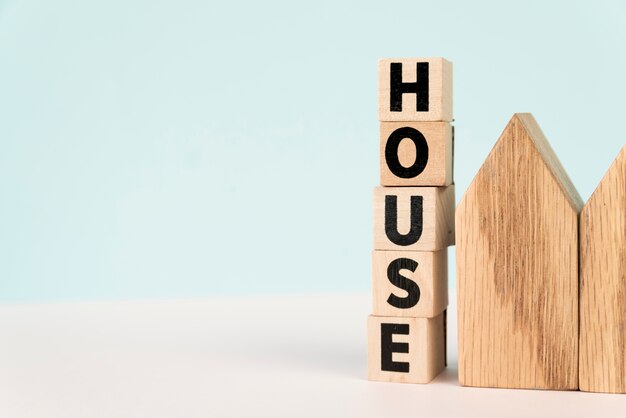 Stacked of letter house blocks near the house model against blue background