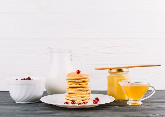 Stacked of small pancakes with red currant berries and lemon curd against white wall