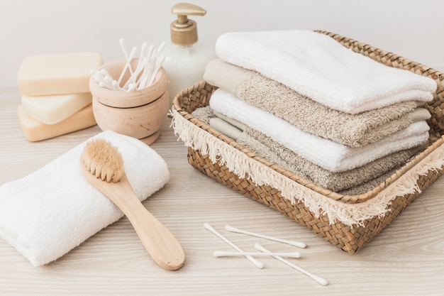 Stacked towels; brush; soap; cotton swab and cosmetic bottle on wooden background