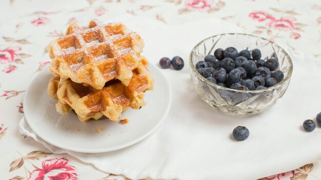Stacked of waffles and bowl of blueberries on tablecloth