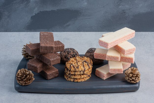 Stacks of wafers and cookies on a navy board with pine cones on marble surface