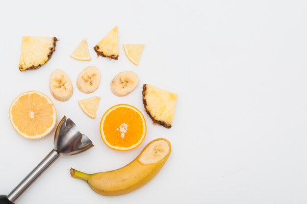 Stainless steel electric hand blender with slices of pineapple; banana and oranges fruits on white background