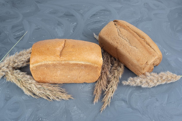 Stalkts of dried feather grass and bread loaves bundle together on marble table.