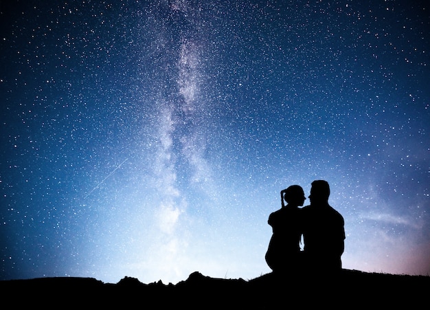 Standing man and woman on the mountain with star light. Hugging couple against purple milky way.