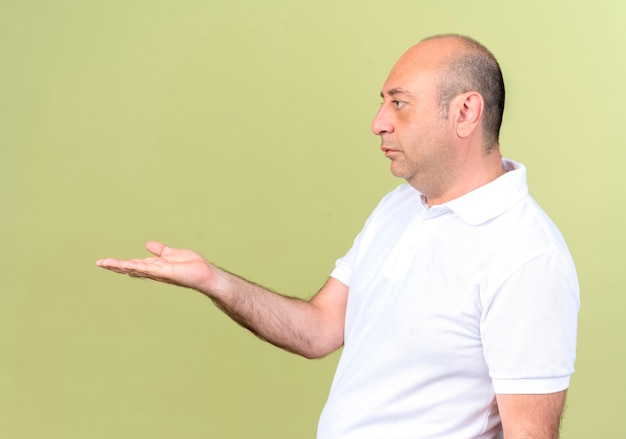 Standing in profile view mature man holding out hand at side isolated on olive green