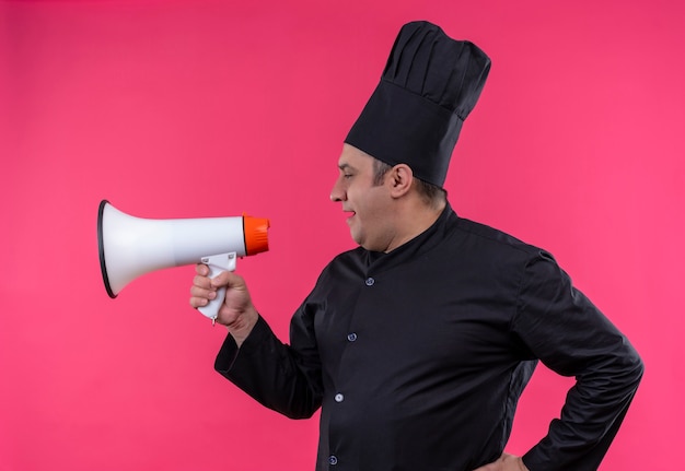 Standing in profile view middle-aged male cook in chef uniform speak through loudspeaker