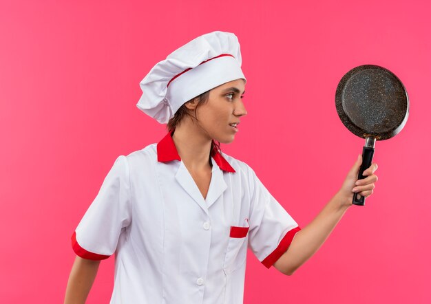 Free photo standing in profile view young female cook wearing chef uniform holding frying pan with copy space