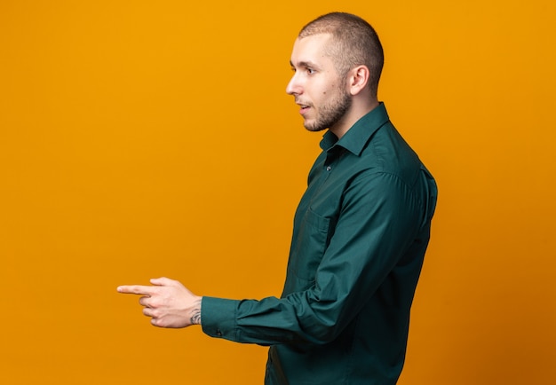 Standing in profile view young handsome guy wearing green shirt points at side 