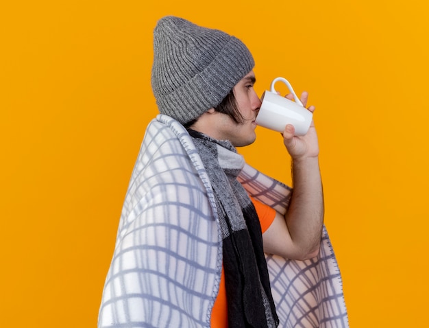 縦断ビューに立って格子縞の飲茶に包まれたスカーフと冬の帽子をかぶっている若い病気の男