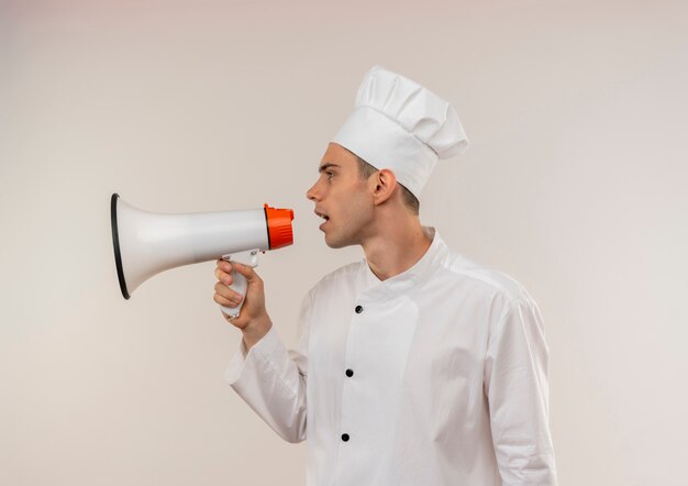 Standing in profile view young male cook wearing chef uniform speake on loudspeaker