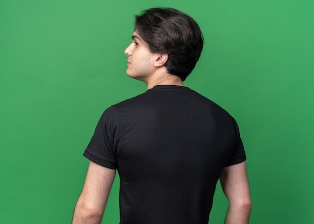 Standing in behind view looking at side young handsome guy wearing black t-shirt isolated on green wall