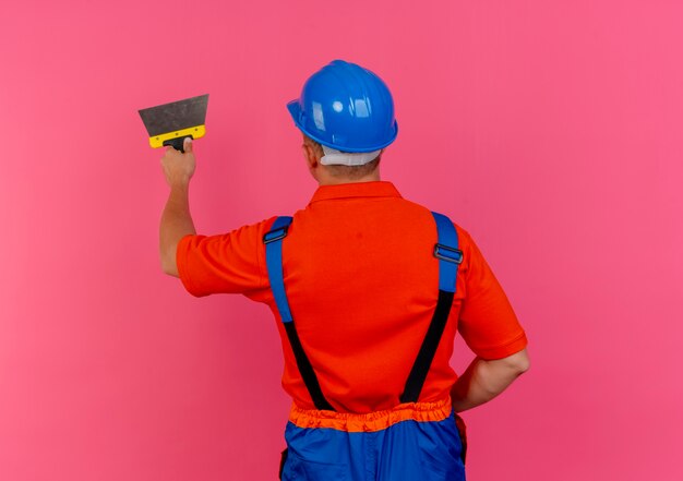 standing in behind view young male builder wearing uniform and safety helmet holding putty knife