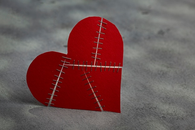 Stapled broken red heart on grey background