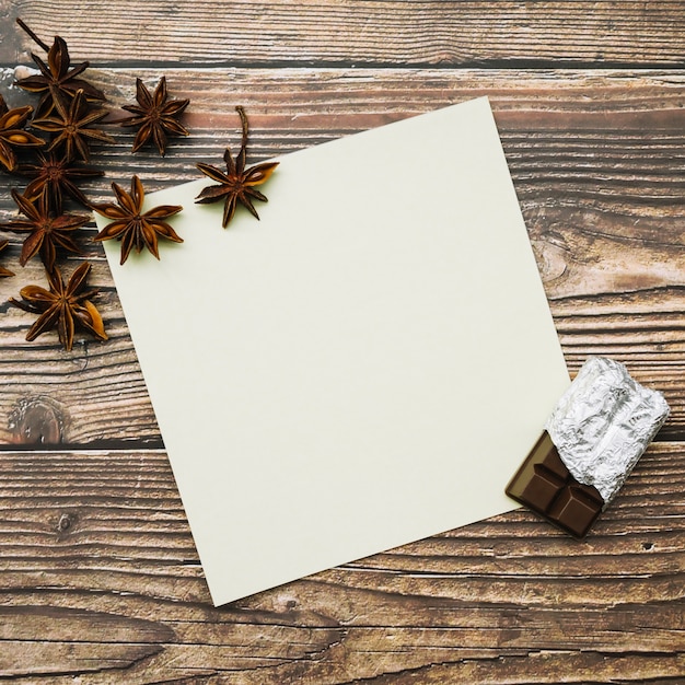 Star anise and chocolate pieces on blank paper over the wooden table