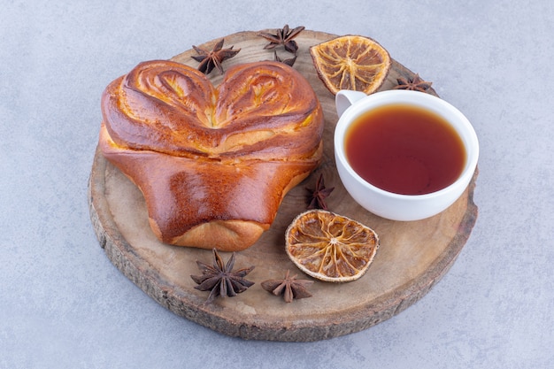 Star anises dried lemon slices, a cup of tea and a sweet bun on a wooden board on marble surface