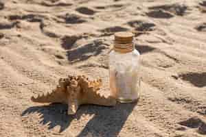 Free photo starfish and glass jar with seashells on sand