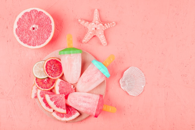 Starfish and scallop shell with grapefruit slices and popsicles on coral textured background