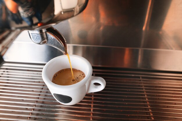 Начните день с чашки ароматного напитка. Стильная черная машина для приготовления эспрессо, заваривающая кофе, снятая в кафе.
