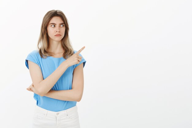 Startled blond woman looking and pointing upper right corner shocked