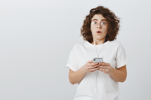 Startled girl stare astounded as holding mobile phone and wearing headphones