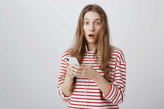 Free photo startled and shocked girl drop jaw, read something online via mobile phone