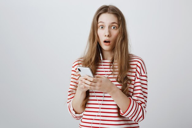 Startled and shocked girl drop jaw, read something online via mobile phone