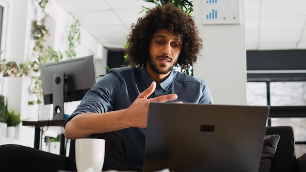 Startup CEO attends business meeting on videocall connection, using online videoconference call to explain company solution for development. Company entrepreneur in open office. Tripod shot.