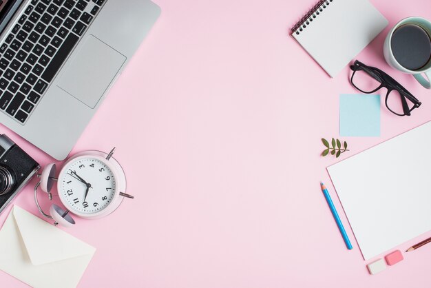 Stationeries; laptop; camera; envelope; alarm clock and stationeries on pink backdrop