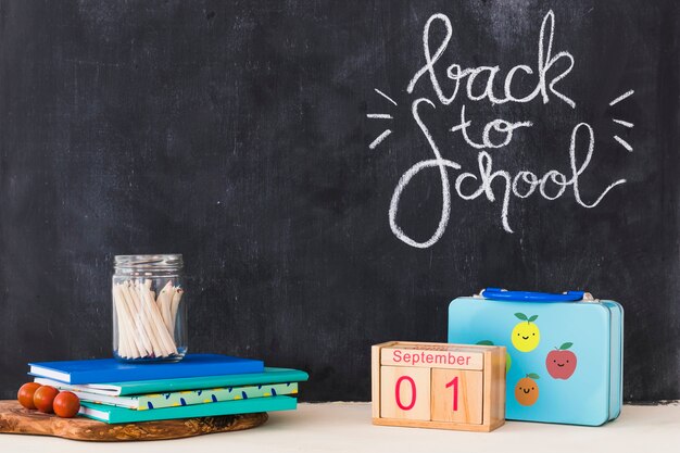 Stationery and calendar lying near lunchbox and blackboard