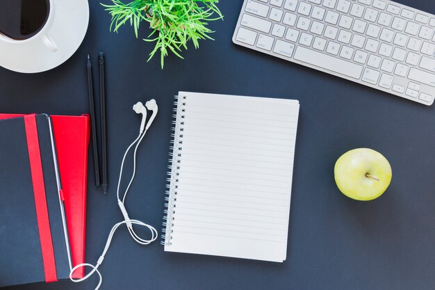 Stationery near coffee cup and apple on table with keyboard