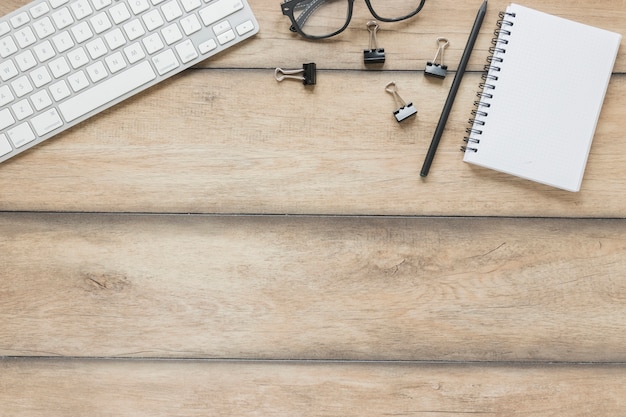 Stationery placed near keyboard and glasses on wooden table