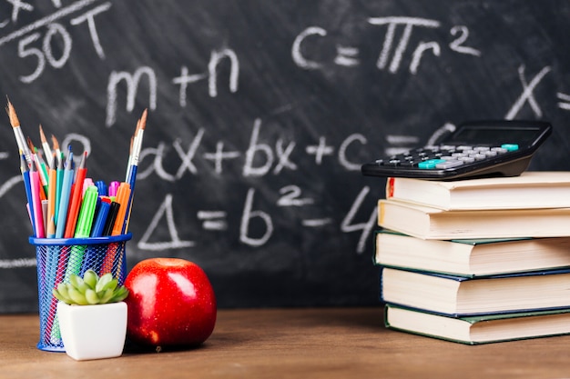 Stationery and stacked books placed on desk on chalkboard background